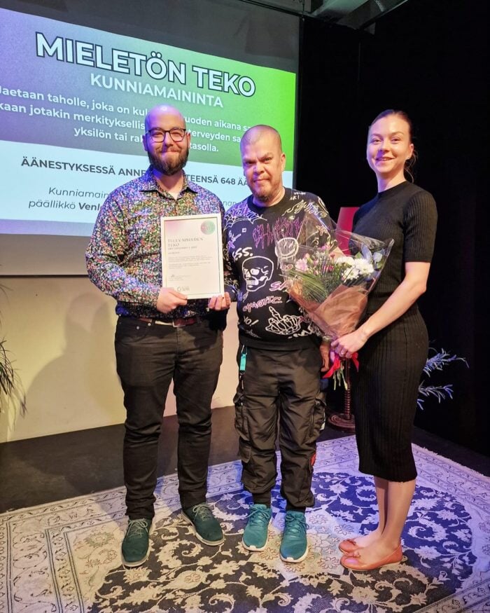 Kuvassa Mika, Tuomo ja Janette noutamassa tulevaisuuden teko -kunniamaininnan palkintoa: kukkia ja taulua.